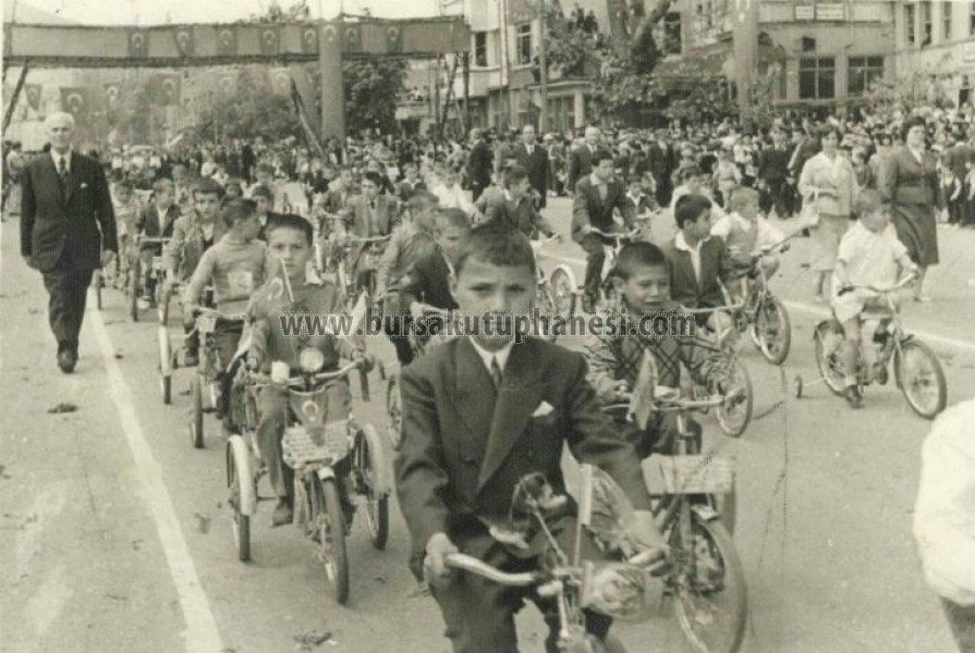 ‎23 nisan 1958. 23 Nisan kutlamaları için Tophane Osmangazi İlkokulu öğrencileri bisikletleriyle tören alanından geçiyorlar. Arka planda Heykel, Hacer Yiğit